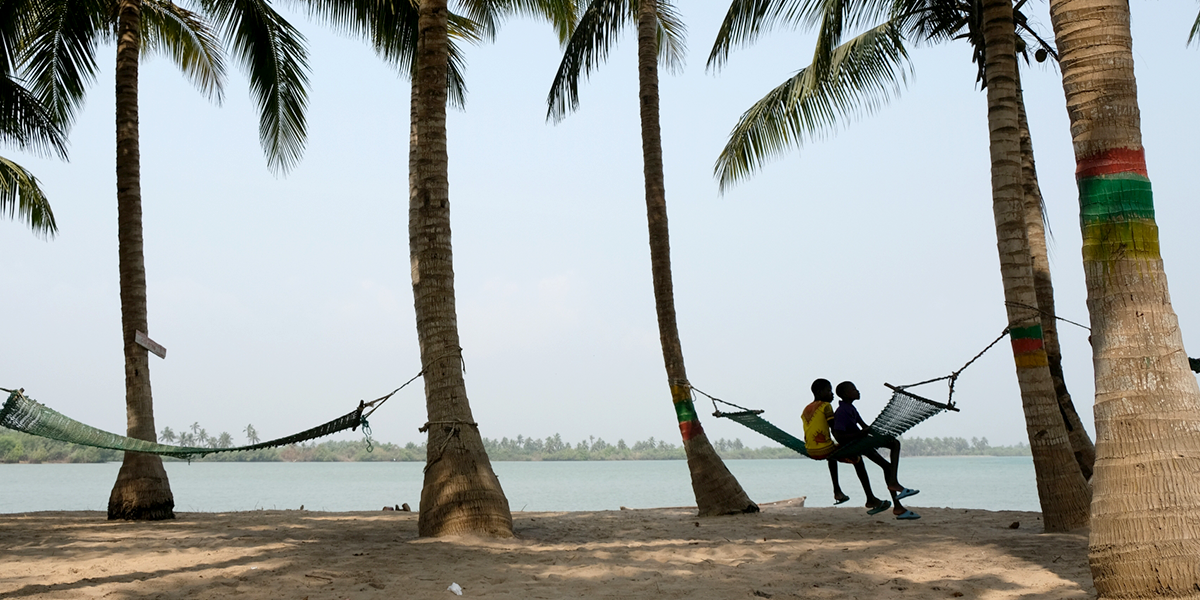 Zwei Kinder in Dogbo, Benin sitzen unter Palmen auf einer Hängematte und schauen in die Ferne