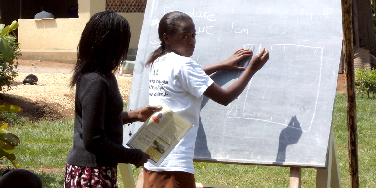 Mädchen steht an einer Tafel und schreibt im Freien in Uganda, Masaka